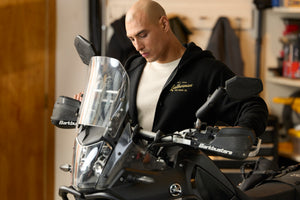 Translation missing: en.A person wearing a black Leatherman Vintage Zip-Up hoodie standing next to a motorcycle in a garage, with the hoodie’s gold Leatherman logo visible on the chest