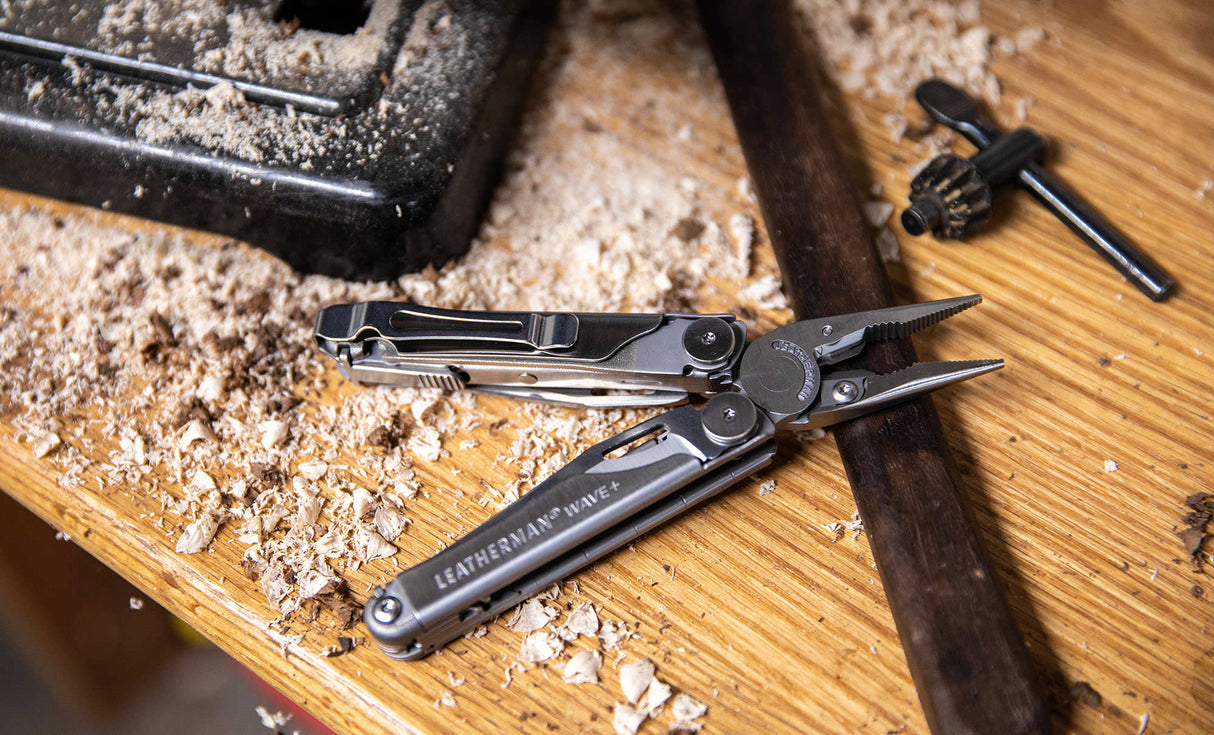 Translation missing: en.Stainless Steel Leatherman Wave® Plus multi-tool on a wood surface with shavings, showcasing its pliers and pocket clip