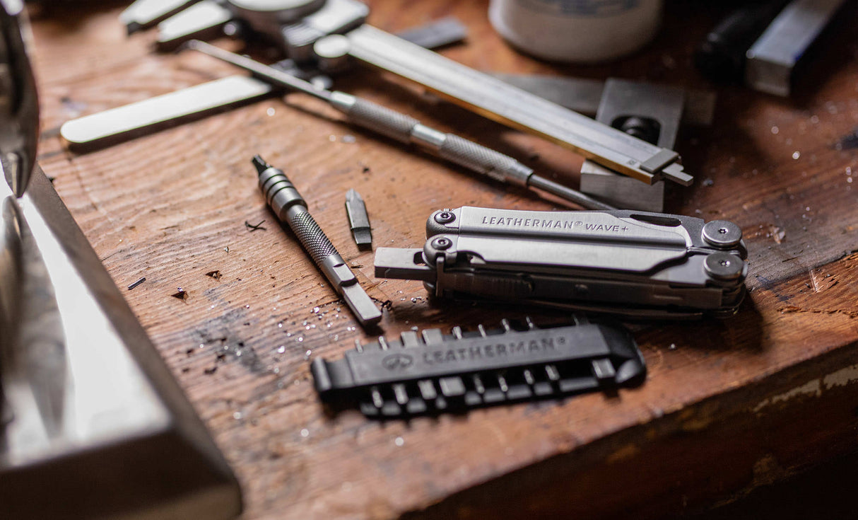 Translation missing: en.Stainless Steel Leatherman Wave® Plus multi-tool on a workbench alongside a Leatherman bit kit, bit and bit driver extender