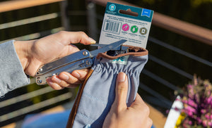 Translation missing: en.Hands using a stainless steel Leatherman Wingman® scissors to cut the zip tie from a garden glove package, showcasing its practicality outdoors